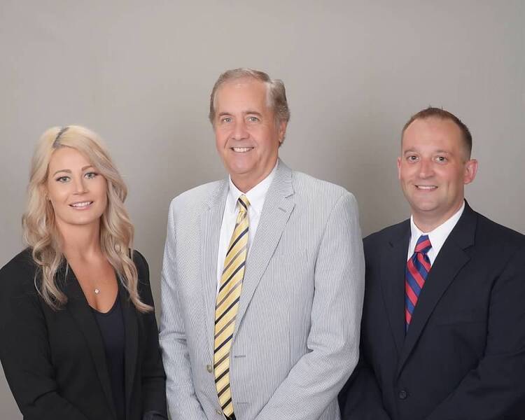 Three white business professionals wearing business suits, standing in front of a gray background.