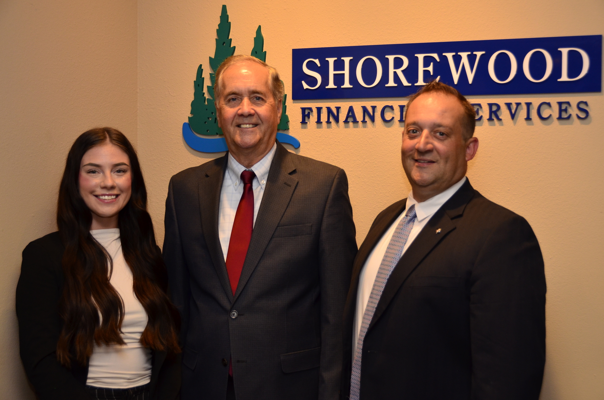 Three white business professionals wearing business suits, standing in front of a gray background.